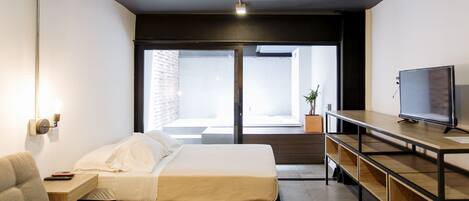 Une chambre d’hôtel moderne équipée d’un lit, d’un coin salon avec un téléviseur et d’une grande fenêtre donnant sur l’extérieur.