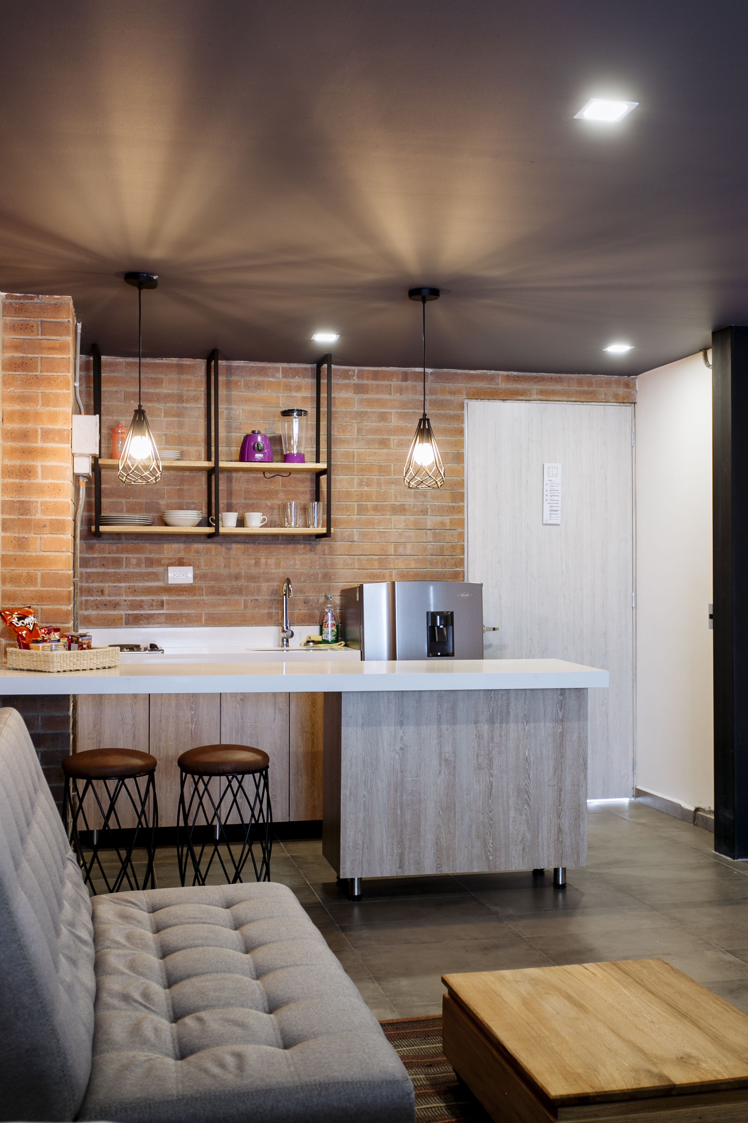 A modern kitchen with a central island, pendant lights, and a brick accent wall.