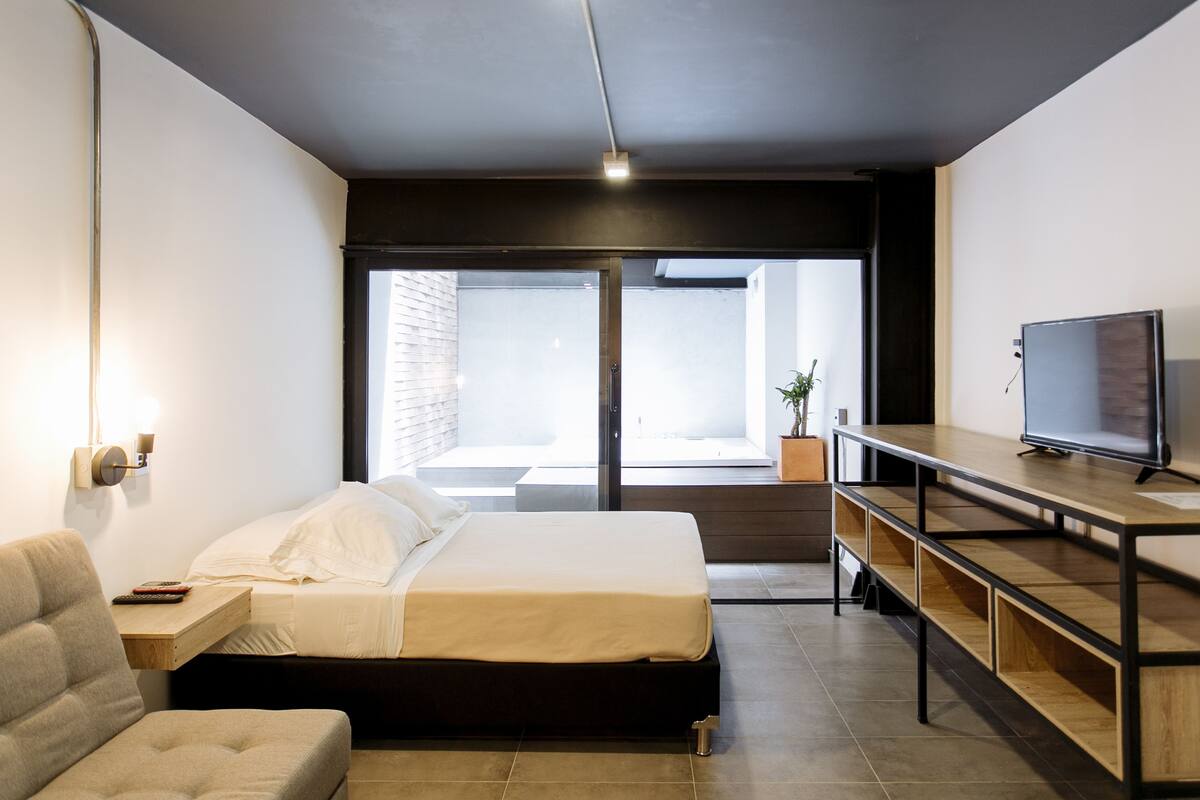 Habitación de hotel moderna con cama, televisor, escritorio y vistas al exterior.