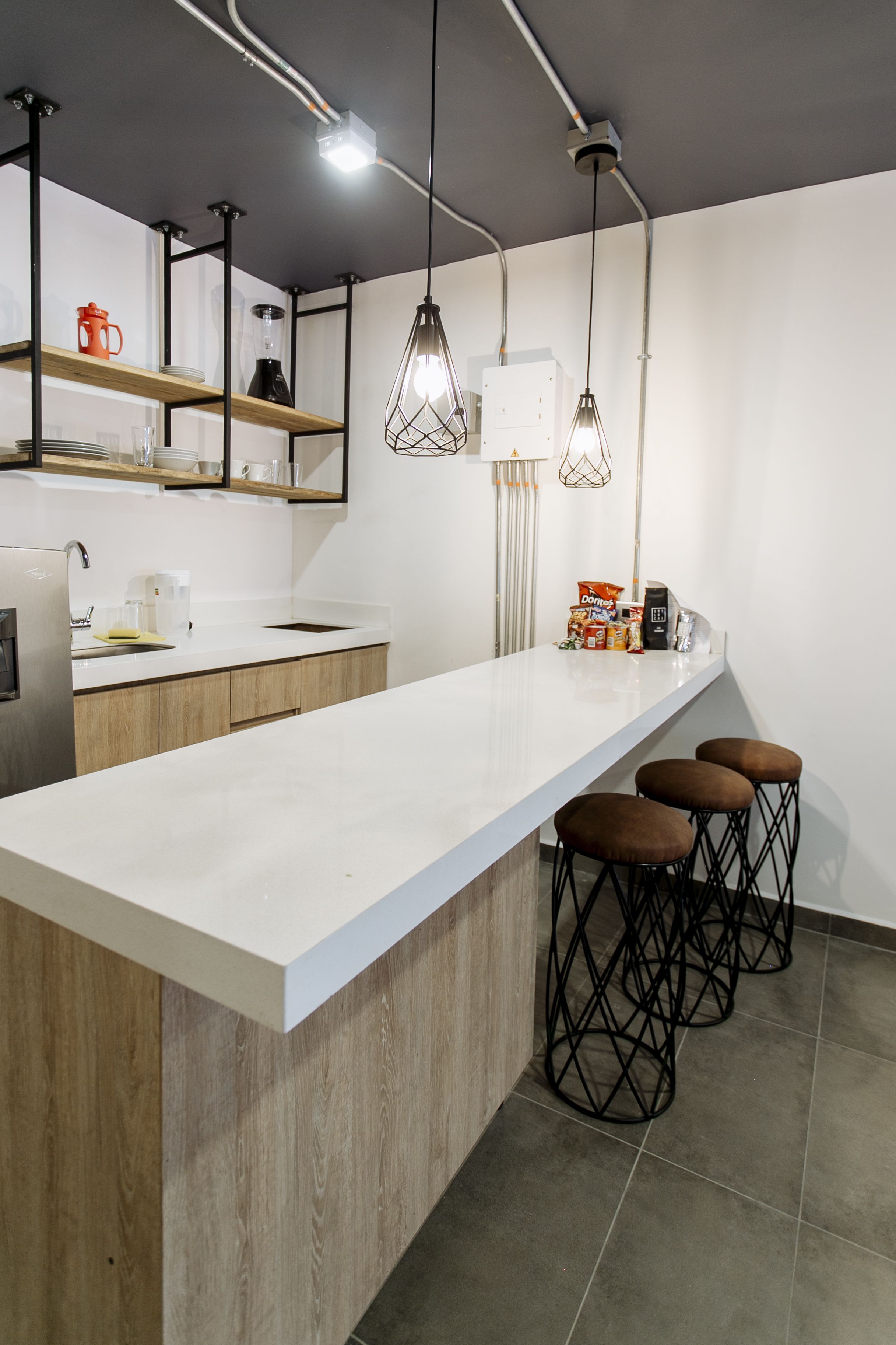 Une cuisine moderne avec un plan de travail blanc, des armoires en bois et trois tabourets de bar.