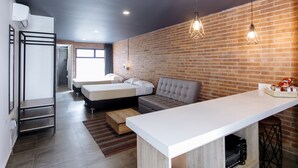 A modern hotel room with a brick wall, a large window, a sofa, a bed, a desk, and a bar area. - Soy Local Provenza (Medellín)