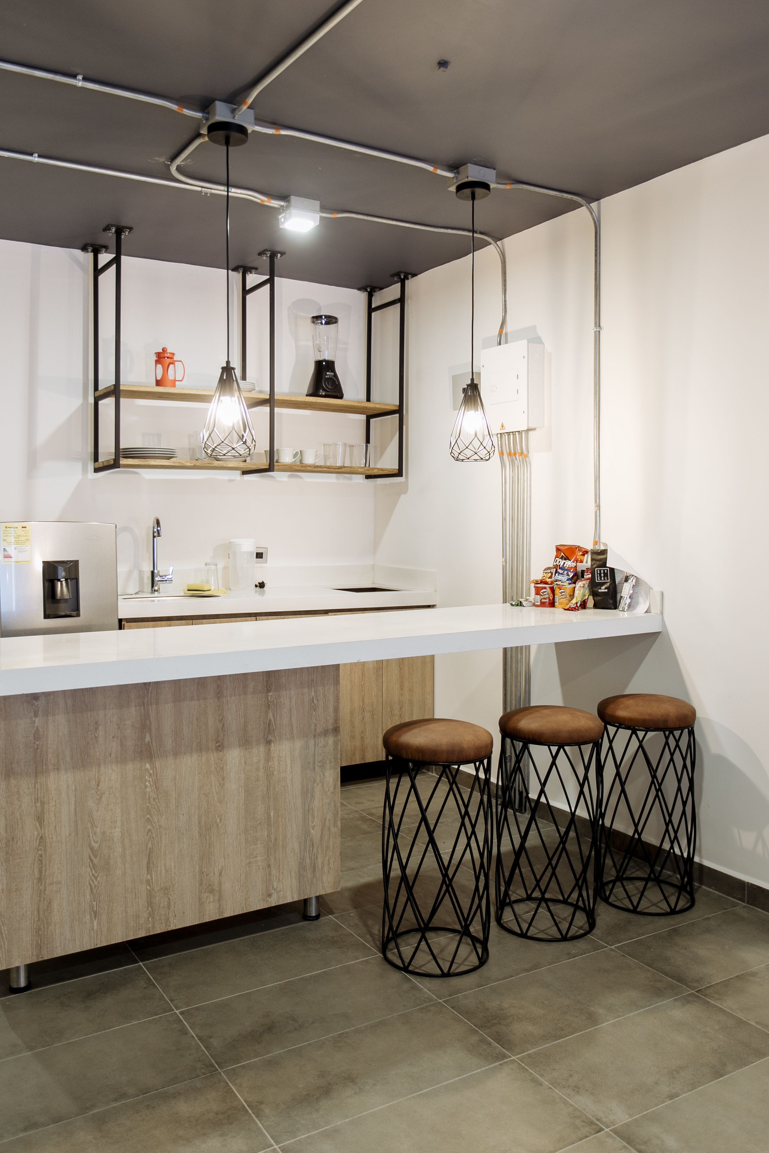 A modern kitchen with a white countertop, wooden cabinets, and three bar stools.