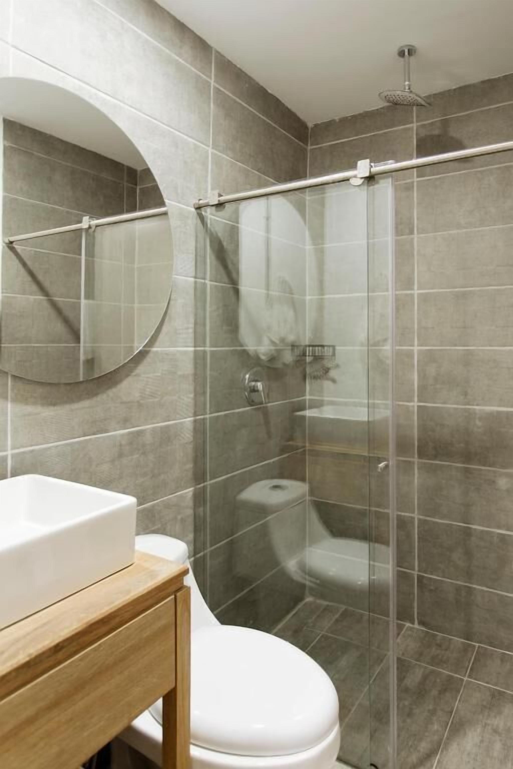 A bathroom with a toilet, a sink, a mirror, and a glass-enclosed shower area.