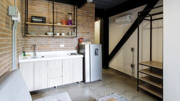 Una cocina compacta con horno integrado, refrigerador y cafetera sobre la encimera.
