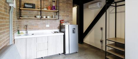 A compact kitchen with a built-in oven, a refrigerator, and a coffee machine on the countertop.