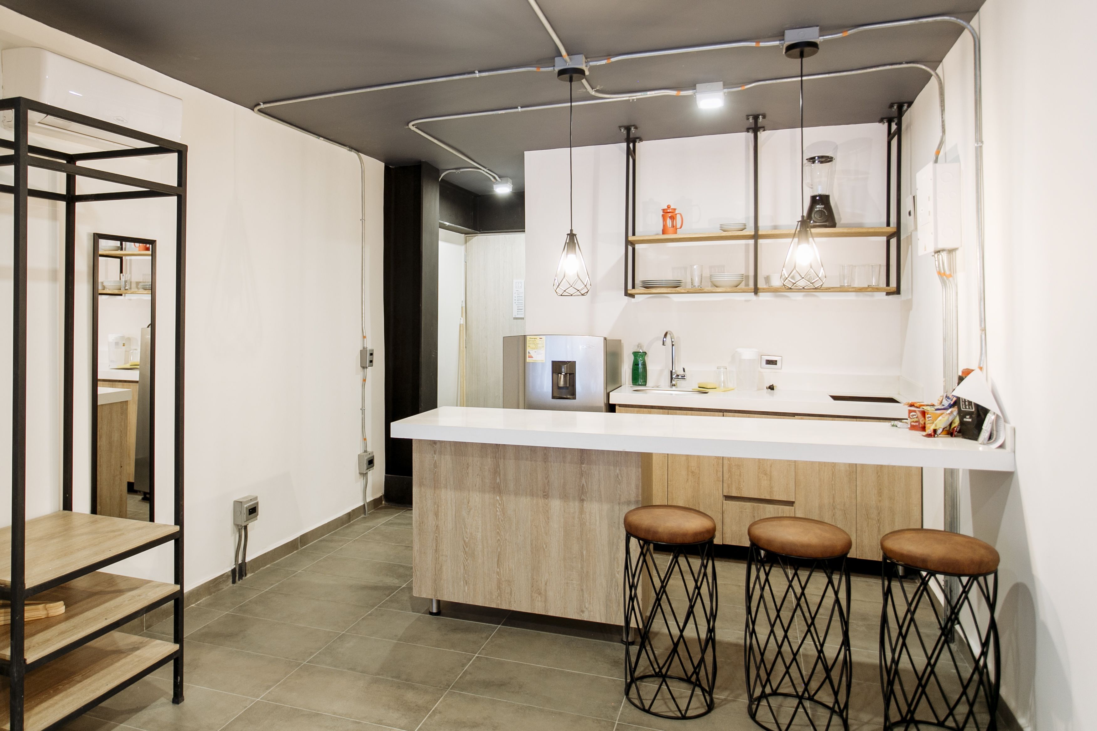 Una cocina moderna con una isla central, taburetes de bar, iluminación colgante y estanterías empotradas.