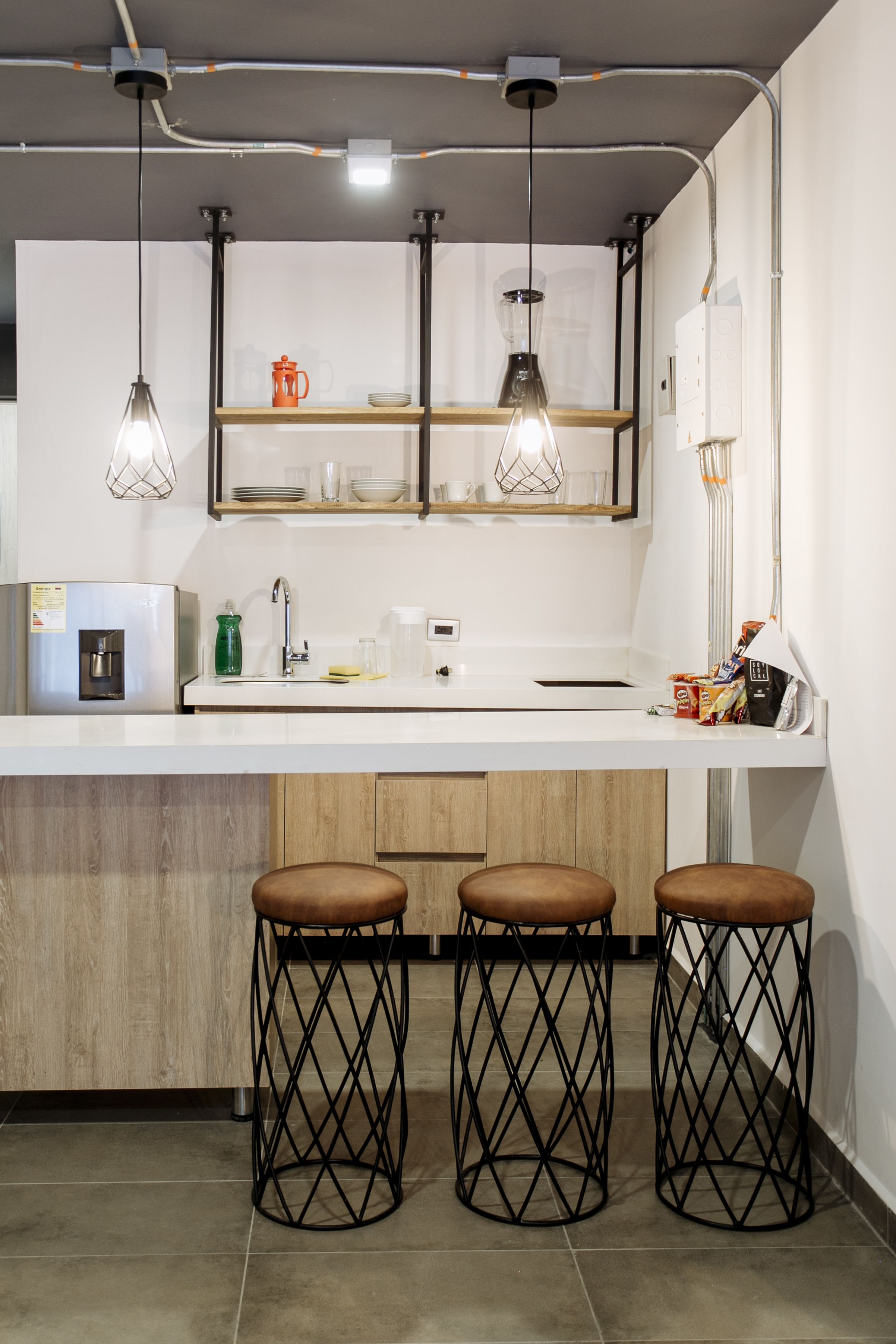 A modern kitchen with a white countertop, stainless steel appliances, and black stools.