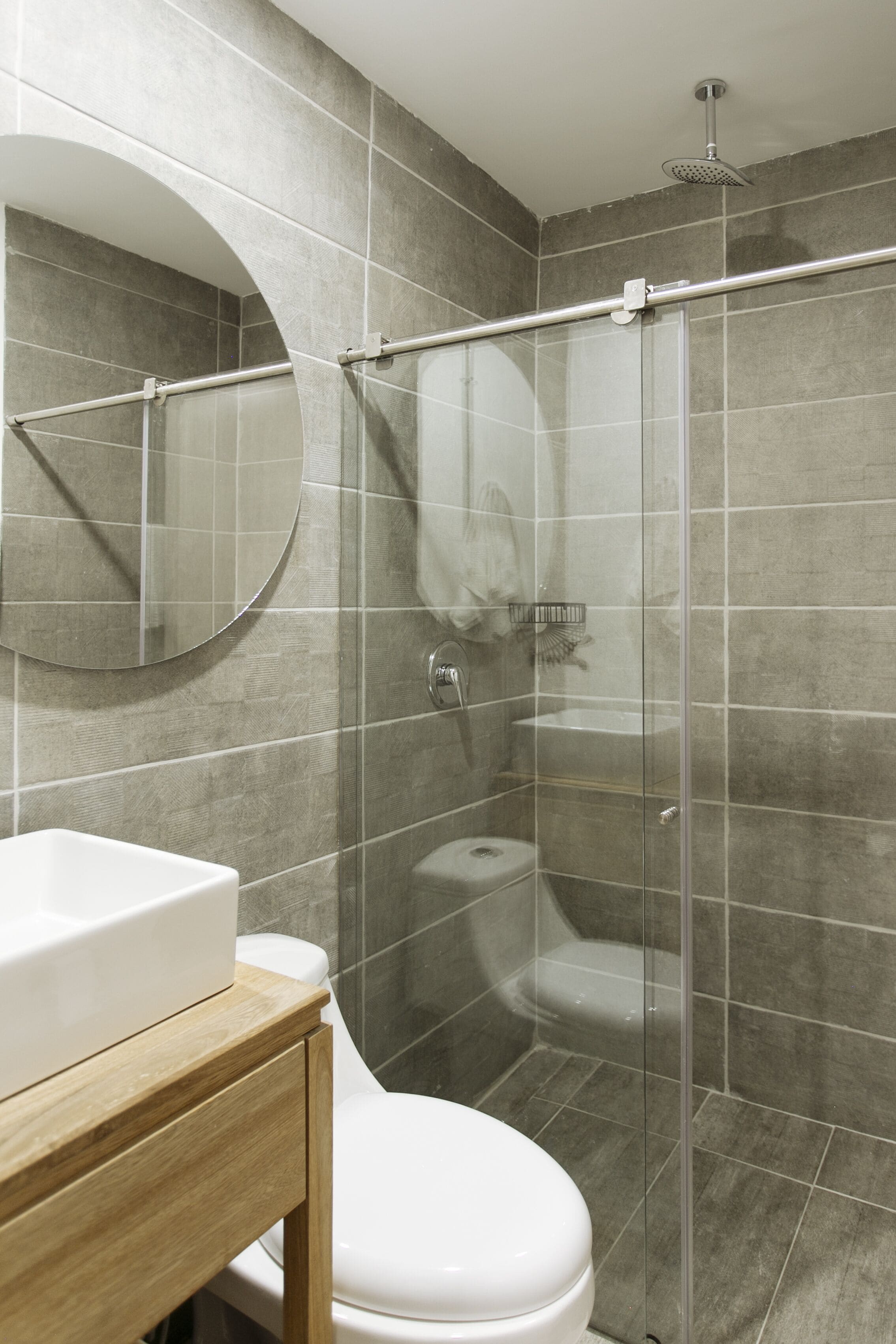 A bathroom with a glass shower enclosure, a toilet, a sink with a mirror, and a wooden vanity.