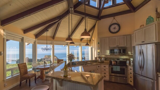 A kitchen with a large island, stainless steel appliances, and a view of the ocean. - Sweetwater Vacation Rentals (Mendocino)