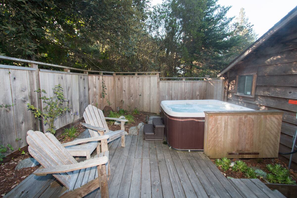 A wooden deck with Adirondack chairs, a hot tub, and a shed.