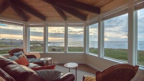 A sunroom with a view of the ocean, furnished with a sofa and two small tables. - Sweetwater Vacation Rentals (Mendocino)