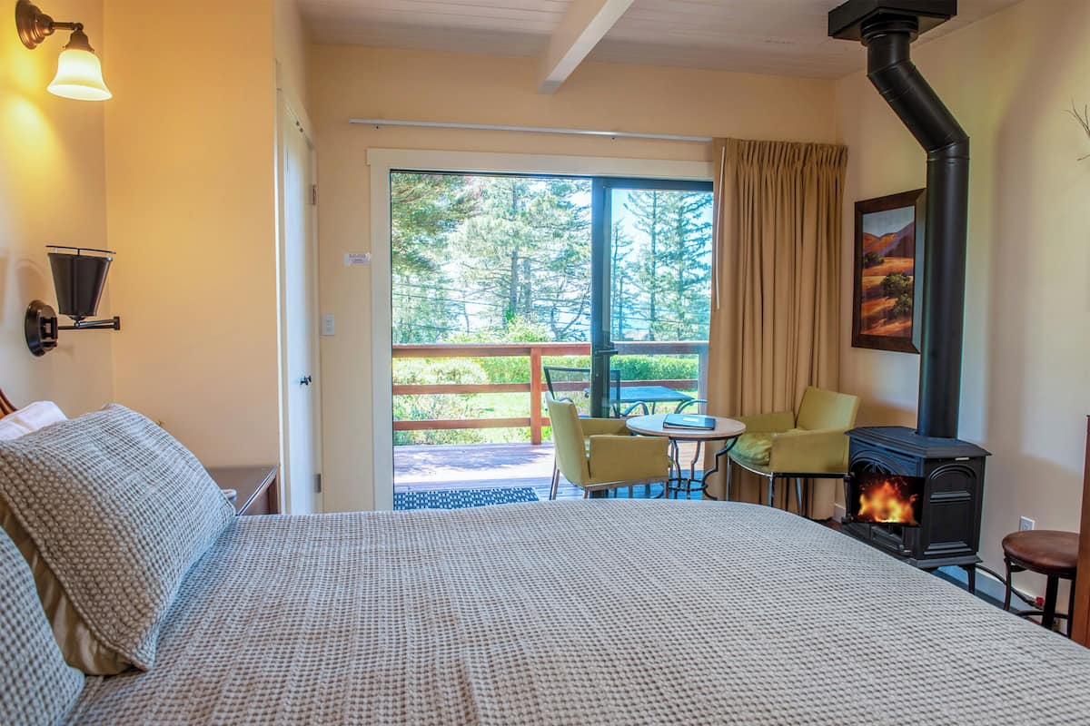 A cozy room with a bed, a table, chairs, a fireplace, and a view of greenery outside.