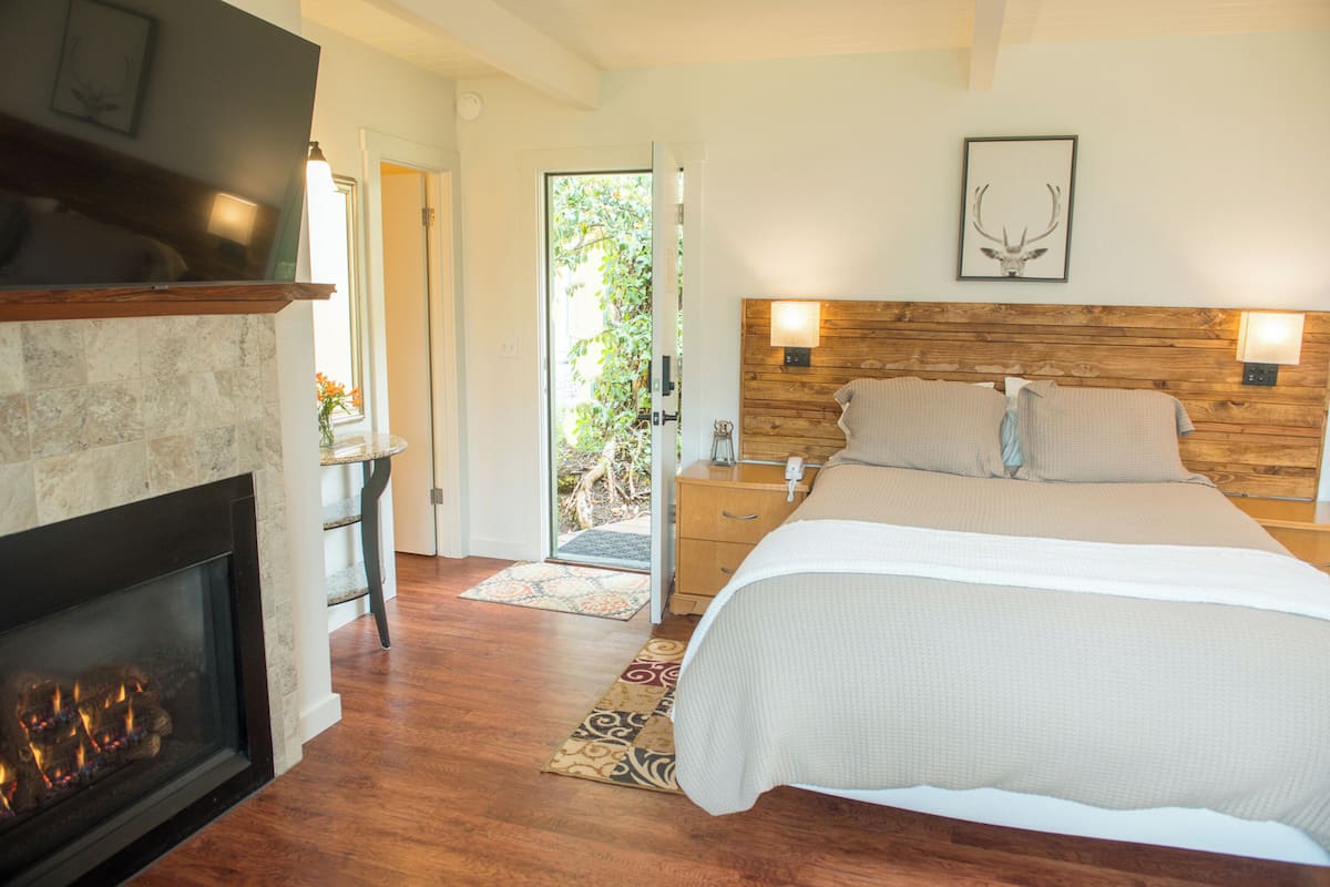 A bedroom with a fireplace, a bed with white bedding, wooden headboard, and two bedside lamps.