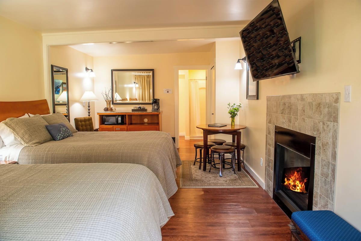 A hotel room with two beds, a fireplace, a desk with a chair, a mirror, and a coffee maker.