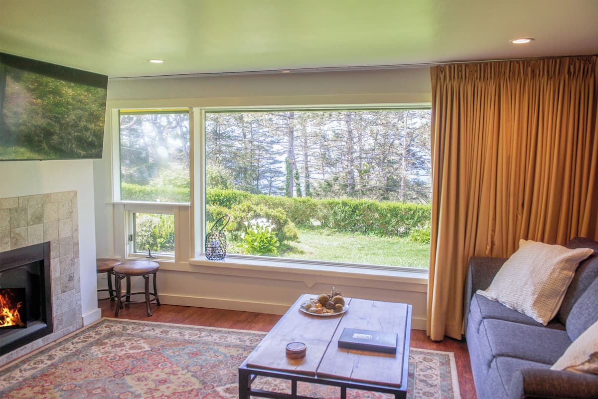 A living room with a fireplace, a large window with a view of trees, a sofa, and a coffee table.