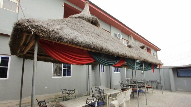 An outdoor seating area with tables and chairs, a thatched roof, and a building with windows and air conditioning units. - Sylva Link Hotel (Lagos)