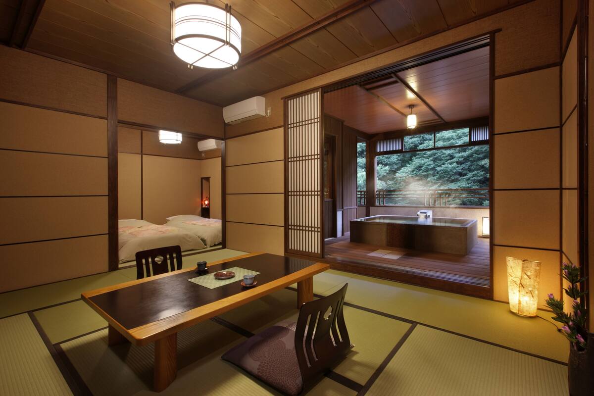 A traditional Japanese room with tatami flooring, a low table, and a sliding door leading to a balcony with a hot tub.