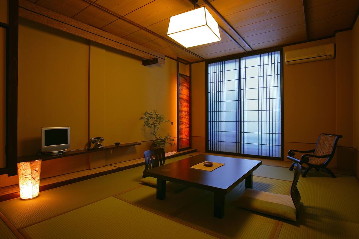 A traditional Japanese room with tatami flooring, a low table, a television, and a sliding door.