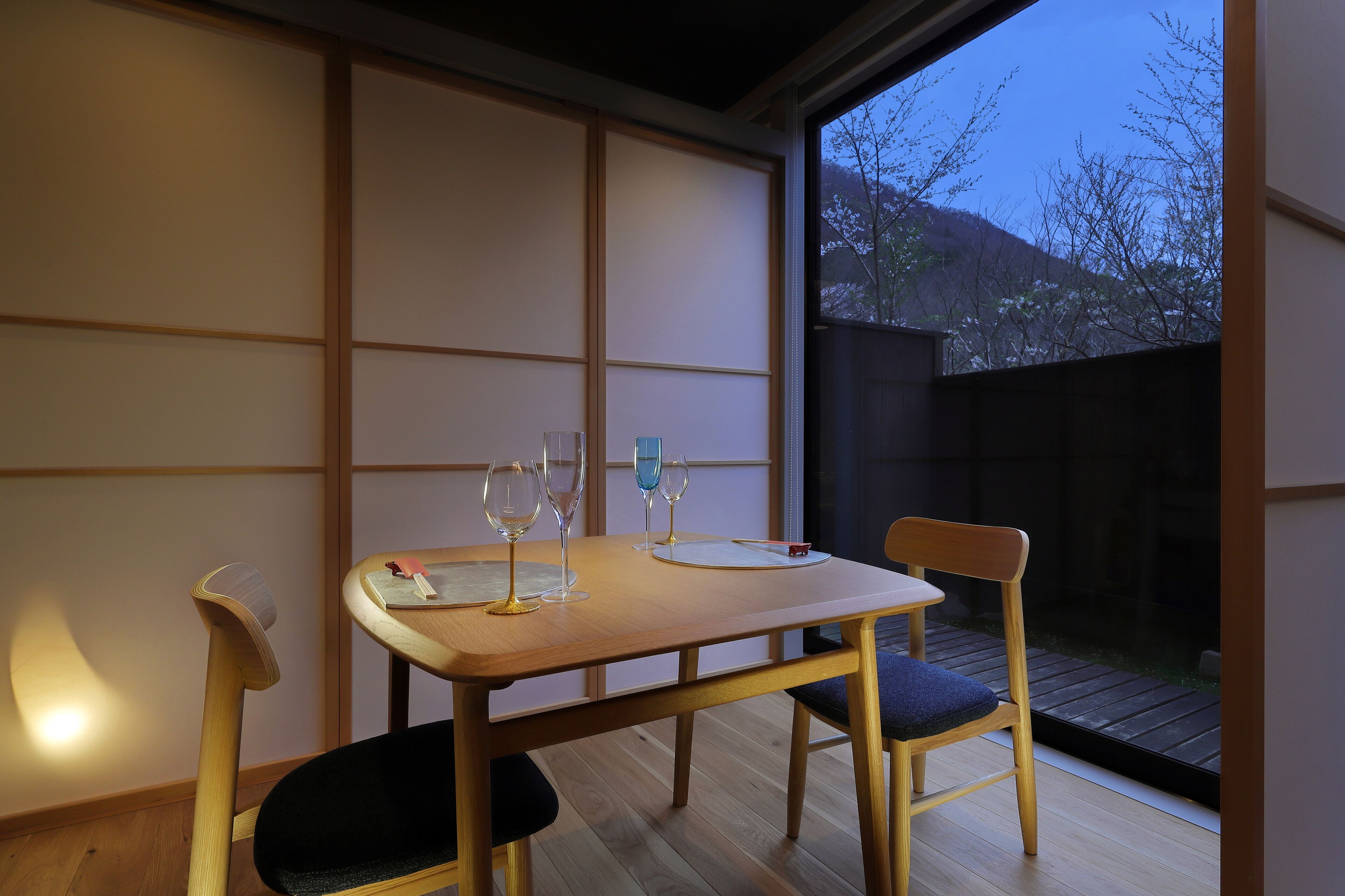 A dining table with three wine glasses and a menu, set in a room with sliding shoji screens and a view of a backyard.