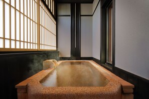 A traditional Japanese onsen with a rectangular hot spring, tiled walls, and a view of the outside through a window with a wooden blind.