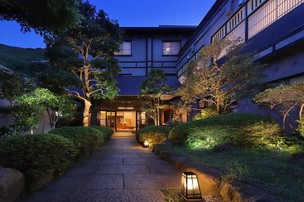 A traditional Japanese building with a well-lit entrance, surrounded by neatly trimmed bushes and trees. - Moritaya (Koriyama)