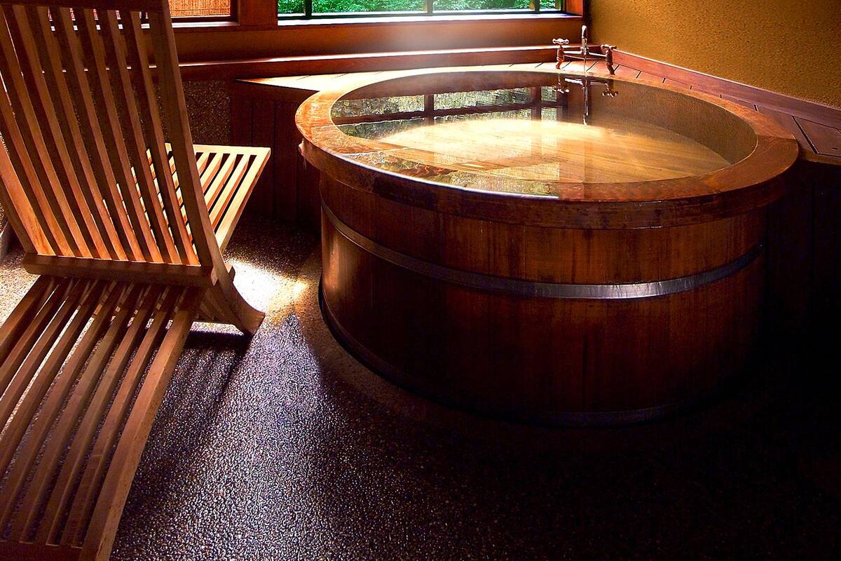 A traditional Japanese room with tatami flooring, a wooden bathtub, and a view of lush greenery through a large window.