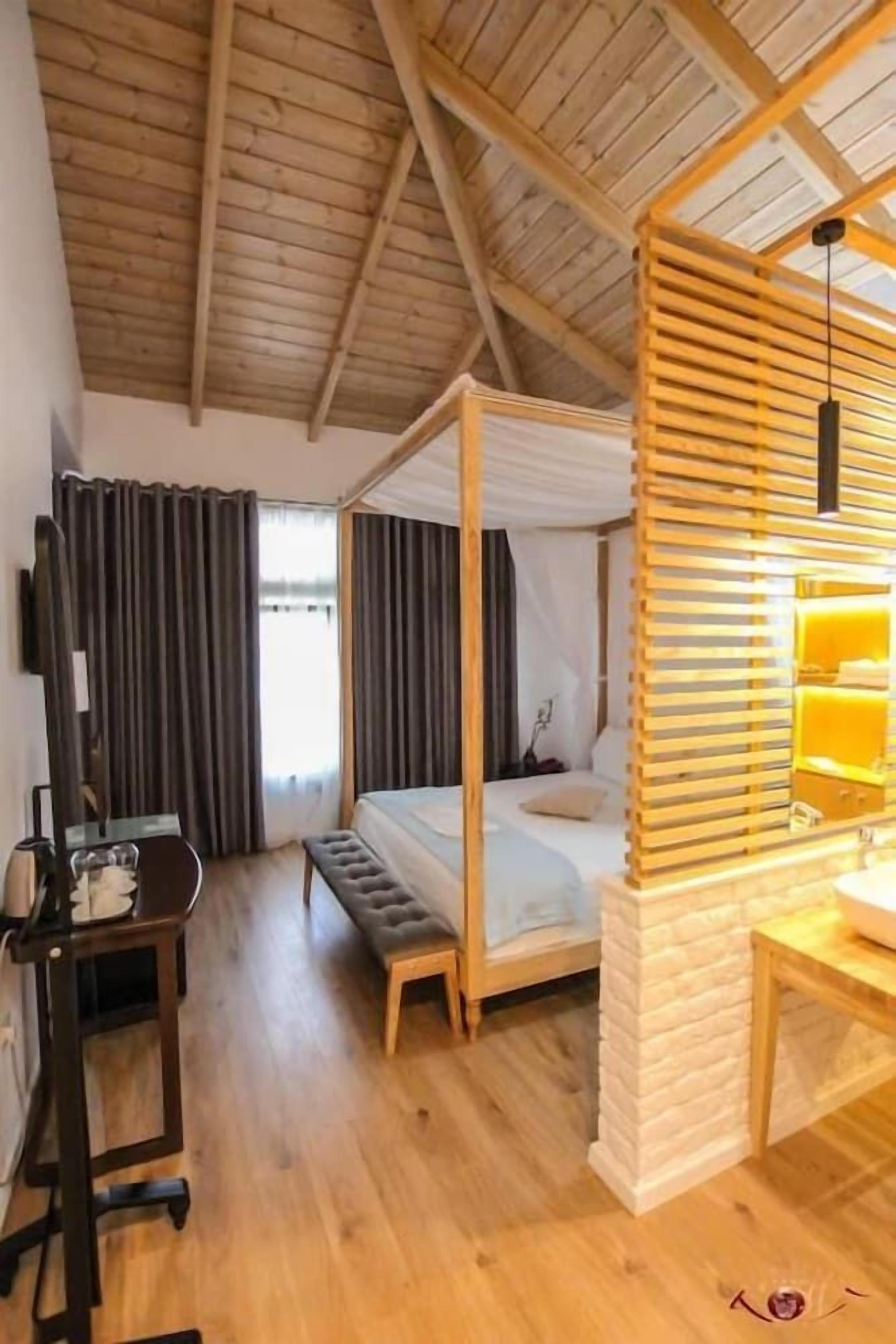 Une chambre dotée d’un lit à baldaquin, d’un bureau avec une chaise, d’une télévision et d’une fenêtre avec des rideaux.