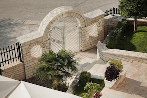 A gated entrance with a stone archway, a palm tree, and a small garden with various plants. - Hotel Vila Sharm (Gjirokaster)