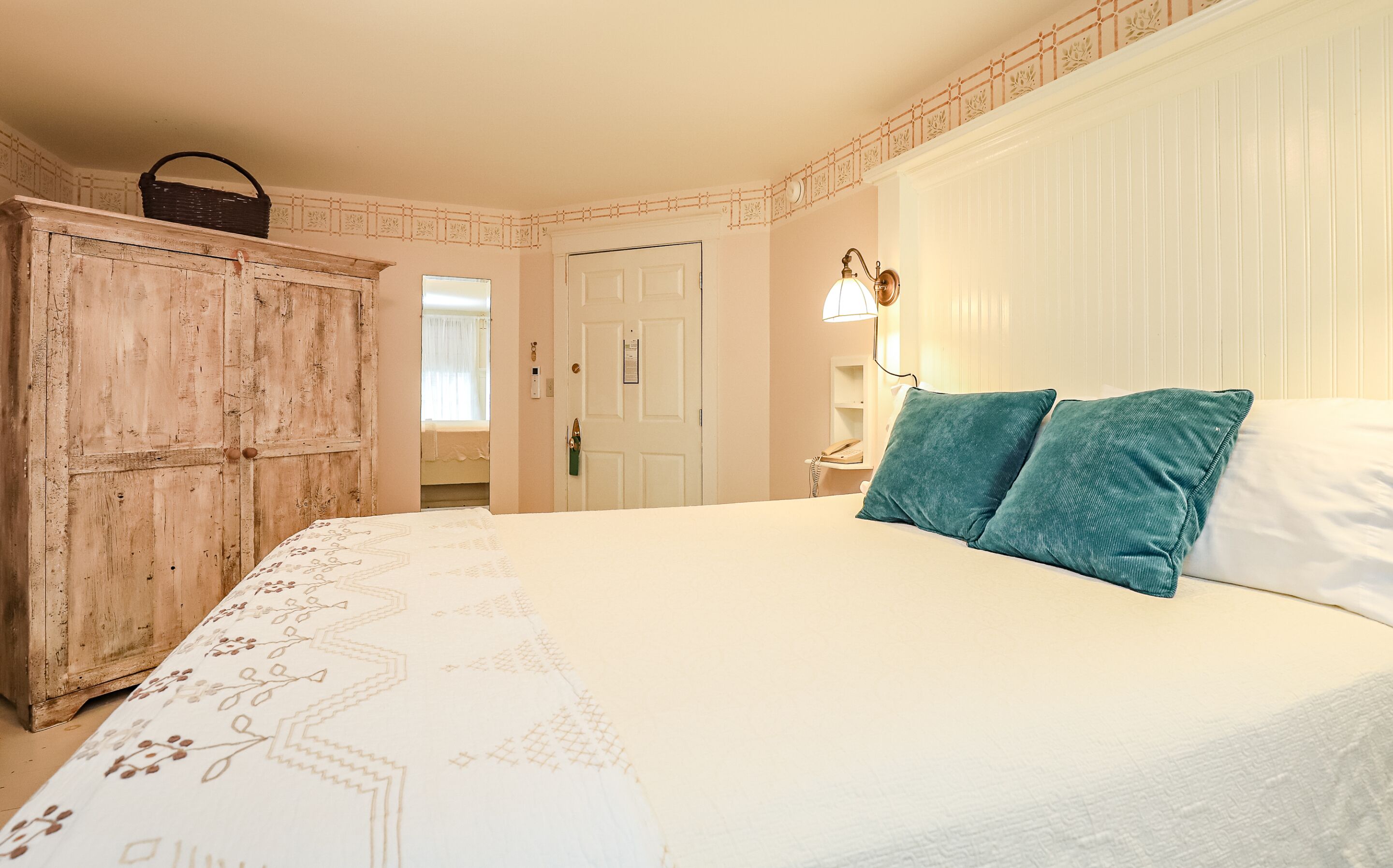 A bedroom with a bed, a wooden wardrobe, a nightstand, and a wall-mounted lamp.