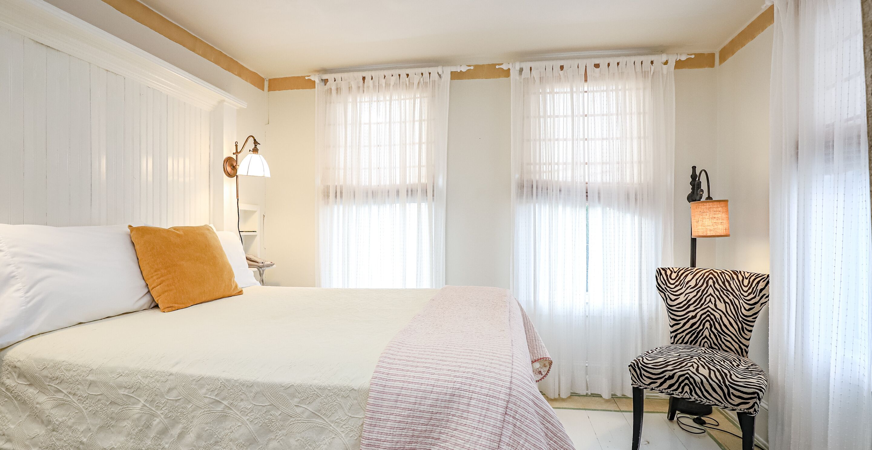 A hotel room with a large bed, a zebra-patterned chair, and two windows with sheer curtains.