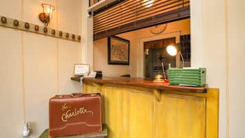 Un área de recepción con mostrador de madera, un reloj, un mapa enmarcado y una maleta antigua con la etiqueta "the Charlotte".