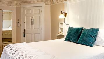 A bedroom with a large bed, a nightstand, a wall-mounted lamp, and a door leading to another room.