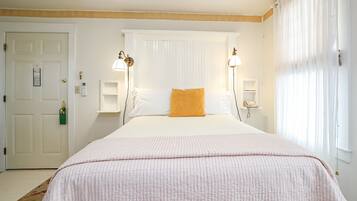 A neatly arranged bedroom with a large bed, two bedside lamps, a window with sheer curtains, and a door with a green keychain.