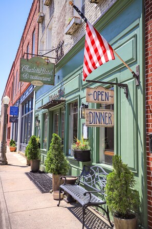 A Charlotte Hotel Restaurant with a green facade, outdoor seating, and an American flag. - The Charlotte Hotel & Restaurant (Onancock)