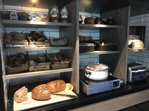 A kitchen with shelves stocked with bread, jars of preserves, and a toaster. - MOXY Stuttgart Airport/Messe (Leinfelden-Echterdingen)