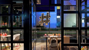 A modern interior with a dining area, a large window with a view of the outside, and a decorative metal sculpture. - MOXY Stuttgart Airport/Messe (Leinfelden-Echterdingen)