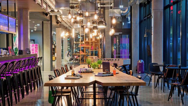 A modern dining area with a long wooden table, black chairs, and hanging pendant lights. - MOXY Stuttgart Airport/Messe (Leinfelden-Echterdingen)