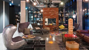 A modern lounge area with a brick accent wall, comfortable seating, a bookshelf, and a jigsaw puzzle table. - MOXY Stuttgart Airport/Messe (Leinfelden-Echterdingen)