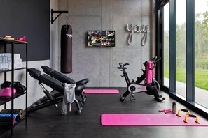 A gym with exercise equipment, a punching bag, and a wall-mounted photo collage. - MOXY Stuttgart Airport/Messe (Leinfelden-Echterdingen)