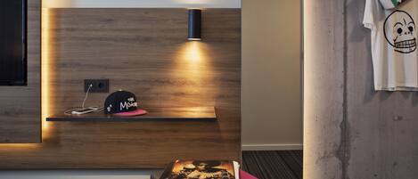 Una habitación moderna con un panel de madera decorativo, una lámpara negra, un taburete rosa y una camiseta blanca con estampado de calavera colgada en la pared.