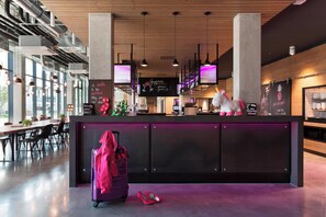 A modern hotel lobby with a reception desk, large windows, and a casual seating area. - MOXY Stuttgart Airport/Messe (Leinfelden-Echterdingen)