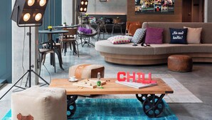 A modern lounge area with a round coffee table, seating, and a bar in the background. - MOXY Stuttgart Airport/Messe (Leinfelden-Echterdingen)