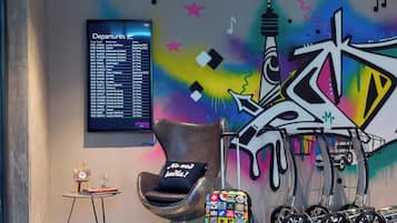 Un área de descanso moderna con un panel de salidas, un mural colorido, una silla original y equipaje.