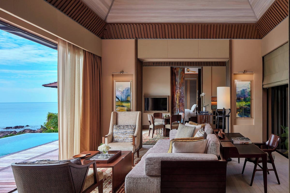 A spacious living room with a large sofa, armchairs, and a dining area. It features a large window with a view of the ocean.