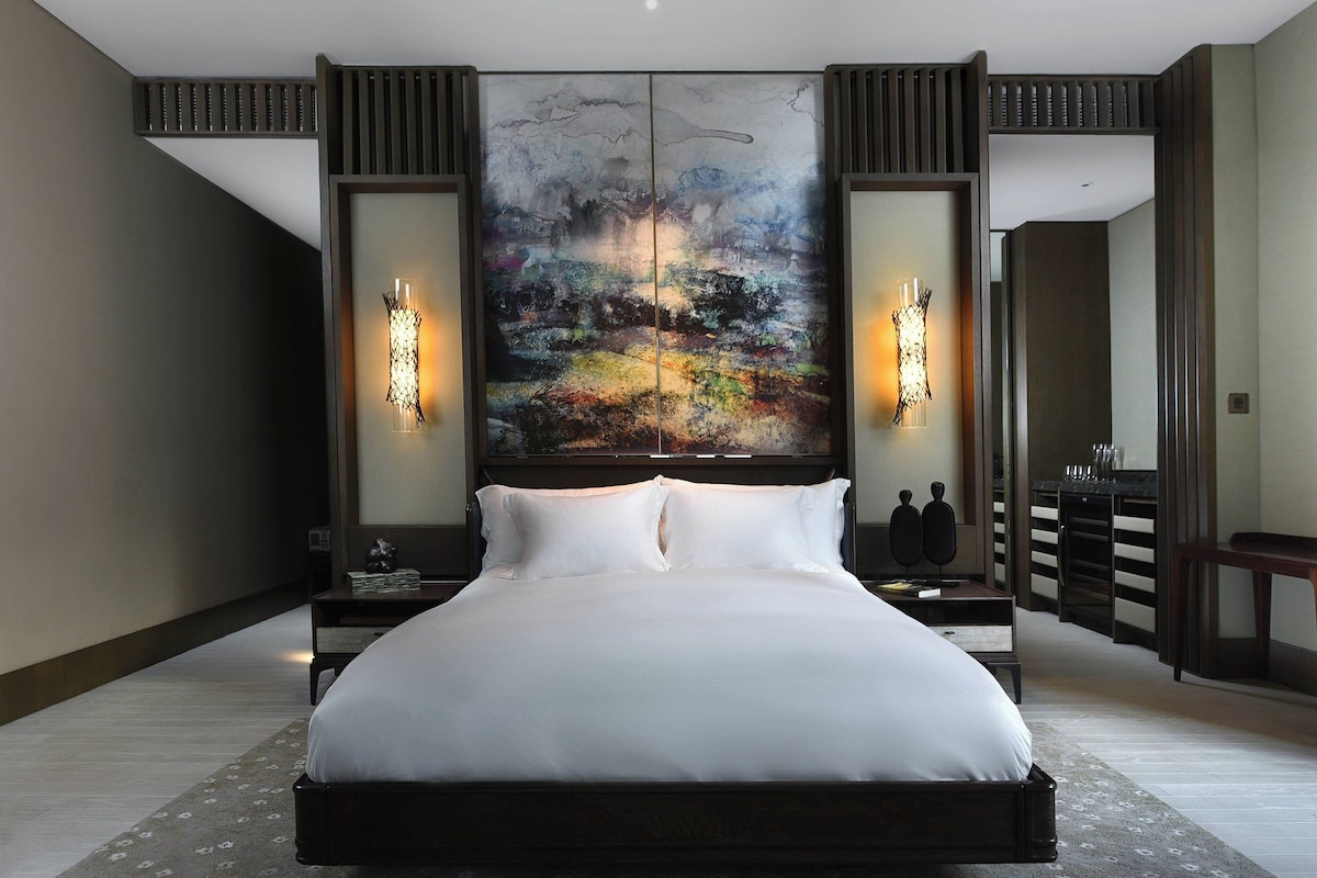 A large bed with white linens in a hotel room. There are two wall sconces with candles on either side of the bed.