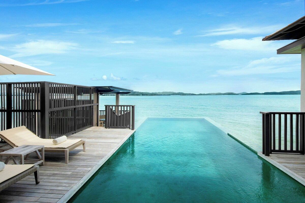 A wooden deck with lounge chairs and a pool extending into the sea.