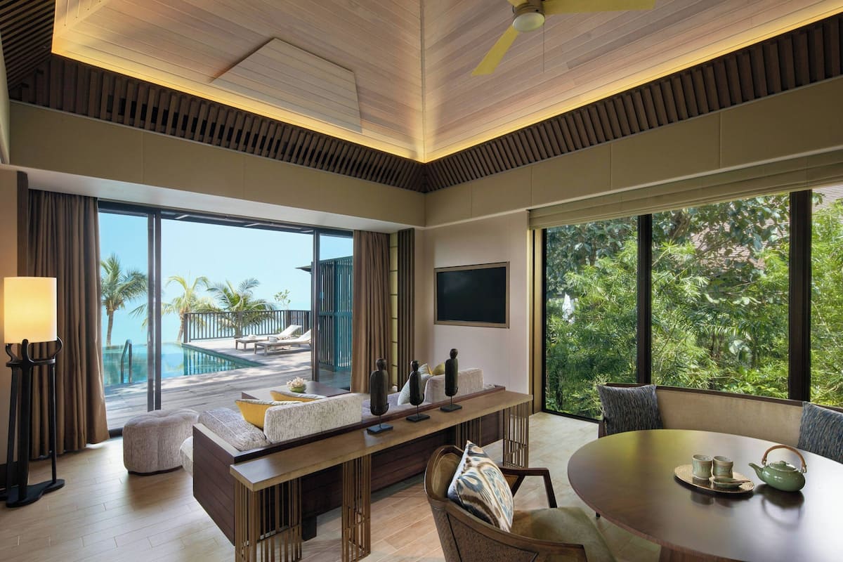 A modern living room with a large window, a pool view, a dining area, and a ceiling fan.
