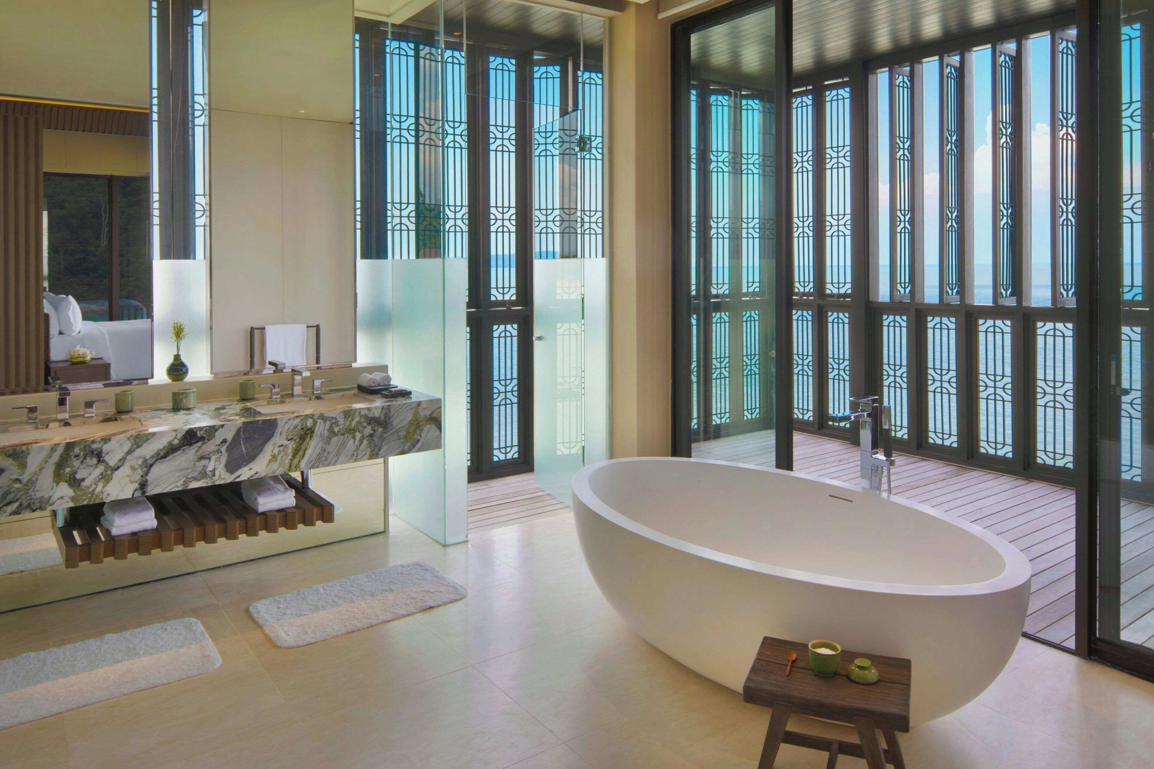 A modern bathroom with a large bathtub, a marble vanity, and large windows with decorative metal grilles.