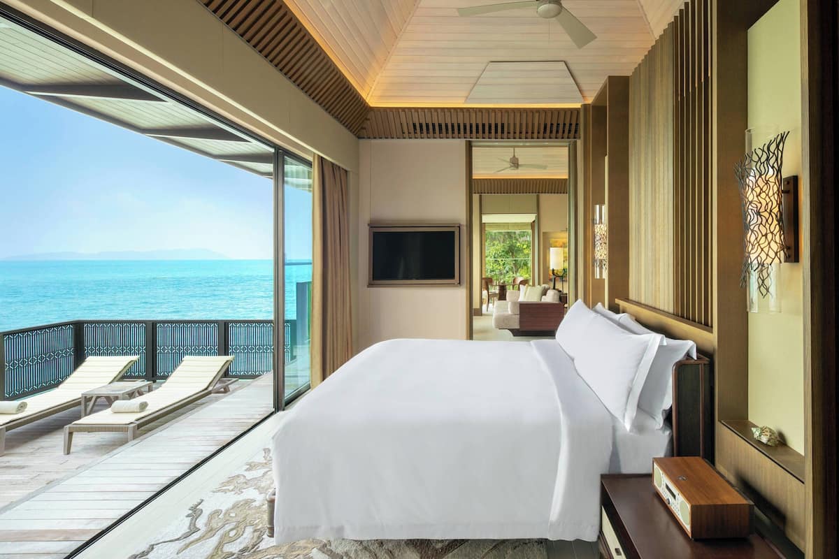 A bedroom with a large bed, a TV, and a balcony with a view of the sea.