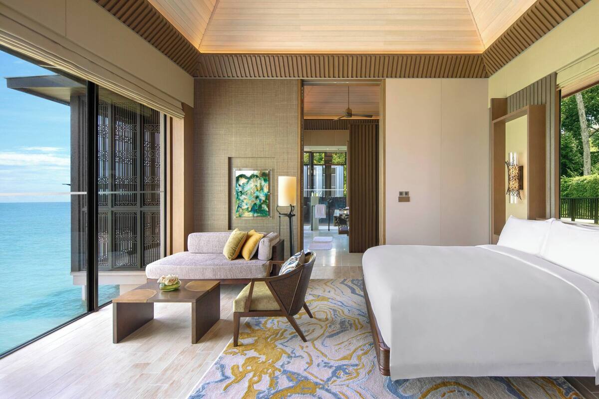 A modern hotel room with a large bed, a sofa, a coffee table, and a view of the ocean.